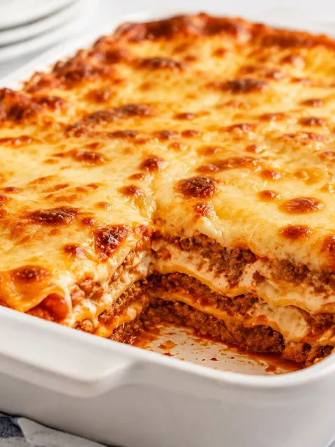 Lasaña gratinada en fuente, con queso dorado y una porción servida